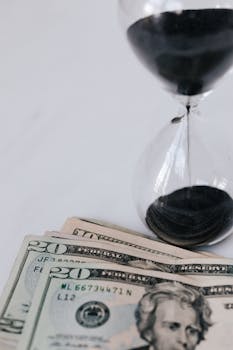 Close-up of an hourglass with dollar bills, symbolizing the connection between time and money.