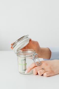 Close-up of hands placing money into a jar, symbolizing savings and financial planning.